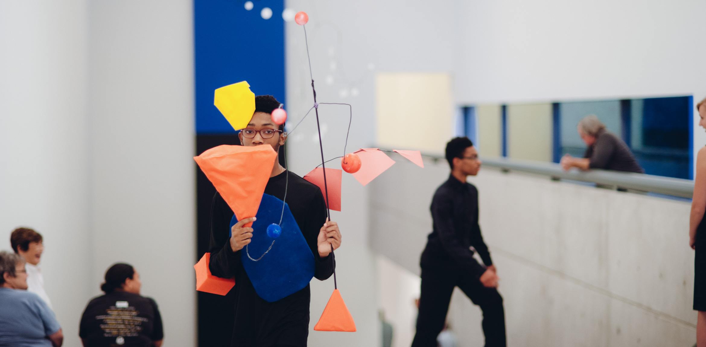 A student performs for an audience in the main gallery holding mobile inspired by Calder's work.