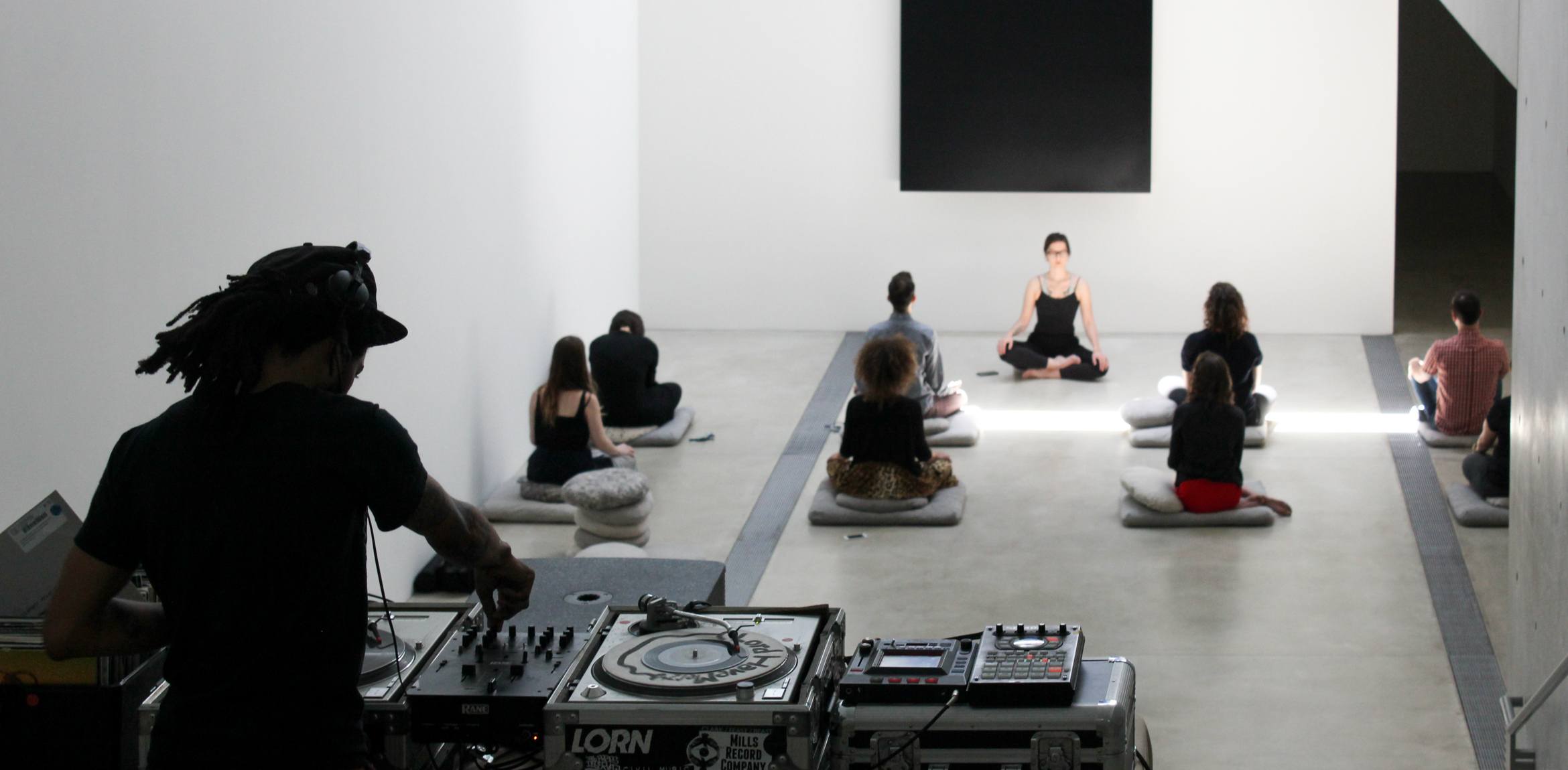 A DJ plays music on the Main Staircase as yoga instructor leads a group of people seated on pillows, in front of Ellsworth Kelly's 