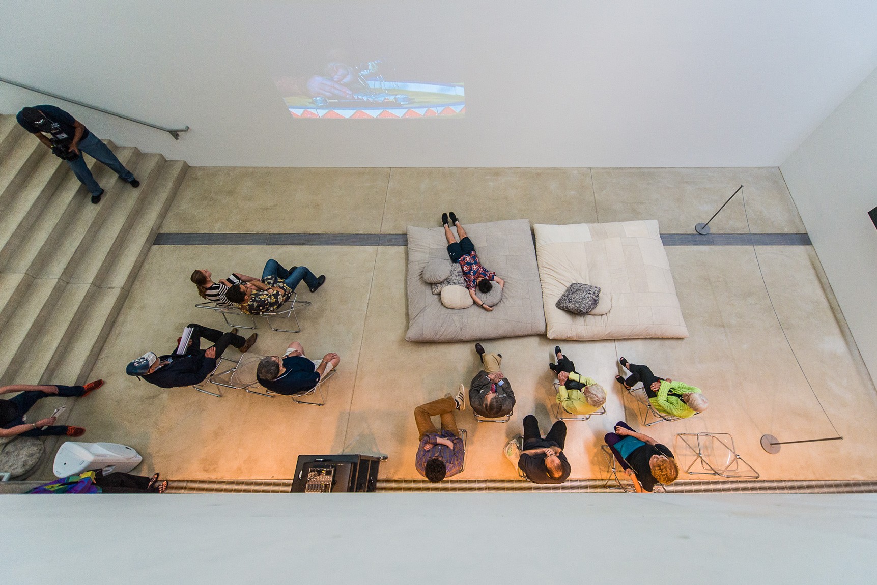 An aerial view of an audience watching a film projected on the wall of the Lower-Main Gallery.