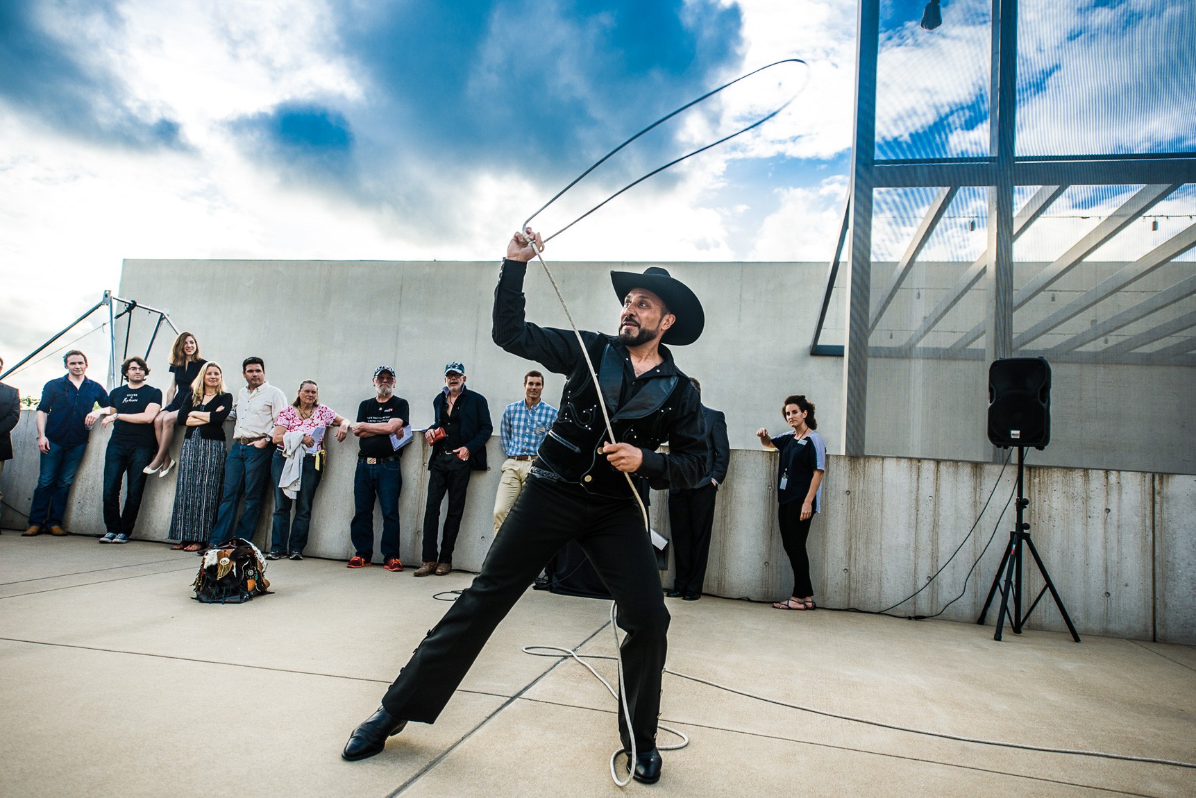 A performer wearing a black western outfit and a cowboy hat swings a lasso for a large audience in the Courtyard.