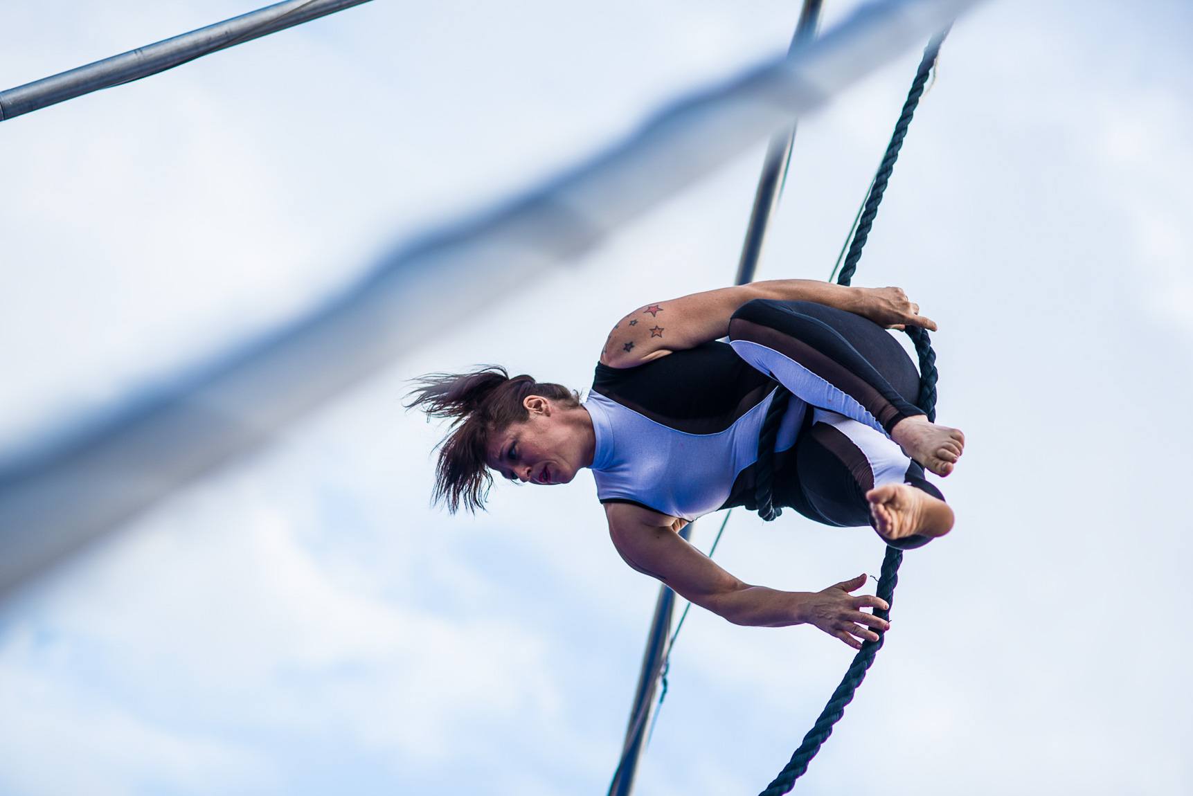 An acrobat twists in the air with a blue rope.