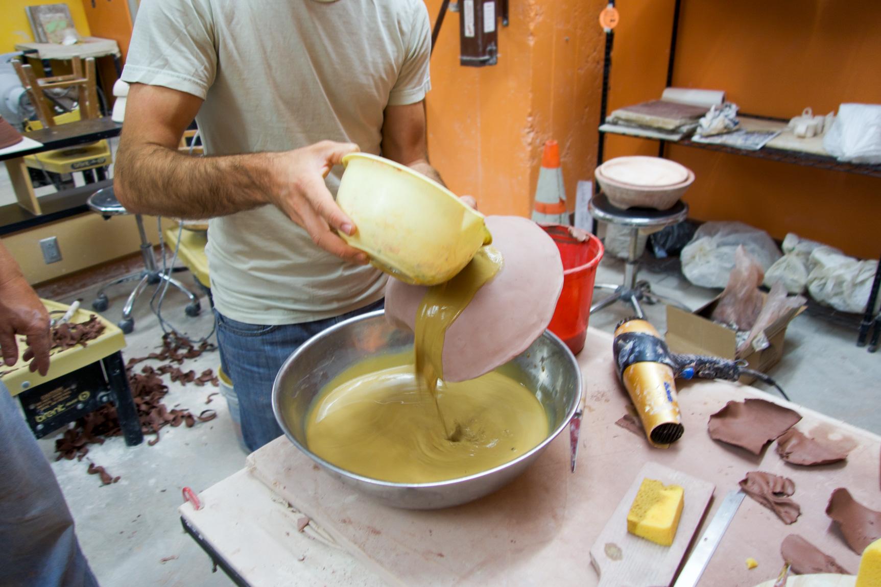 Chris Kallmyer pouring glaze over a clay instrument in his studio.