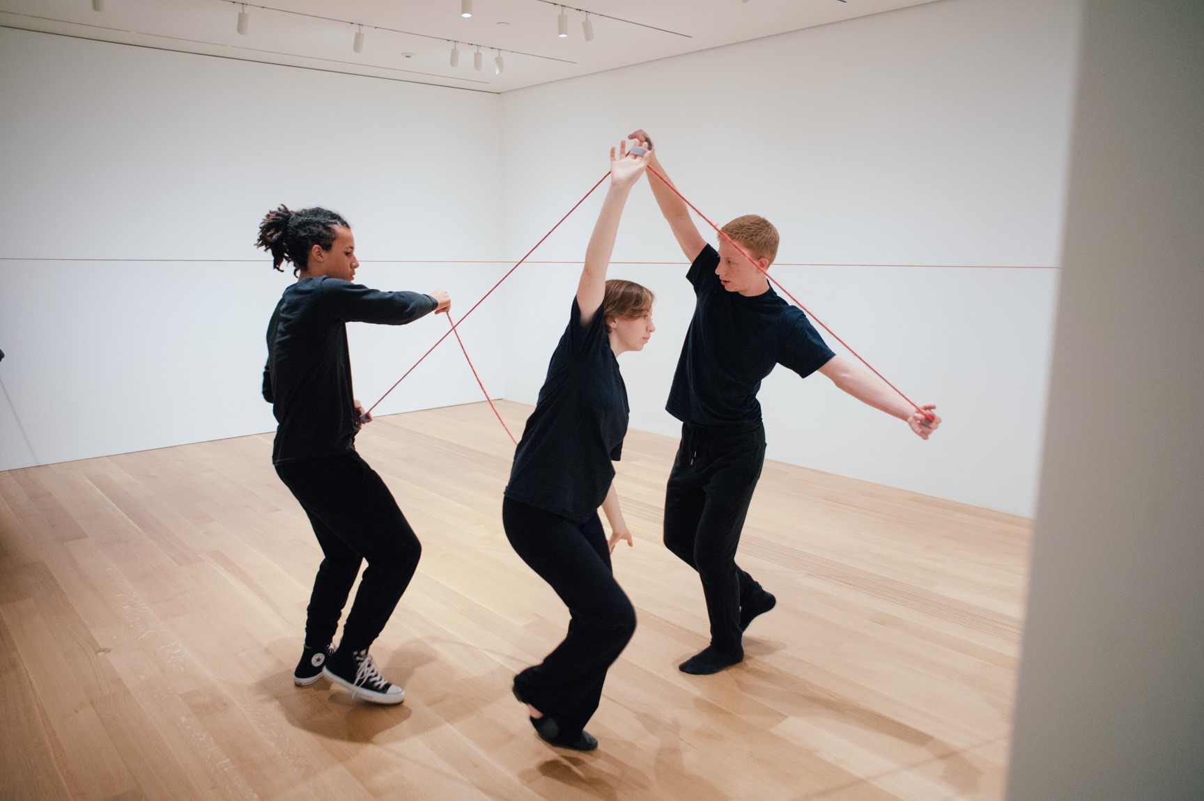 Three students perform the Lower-East Gallery with red ropes tied to their fingers.