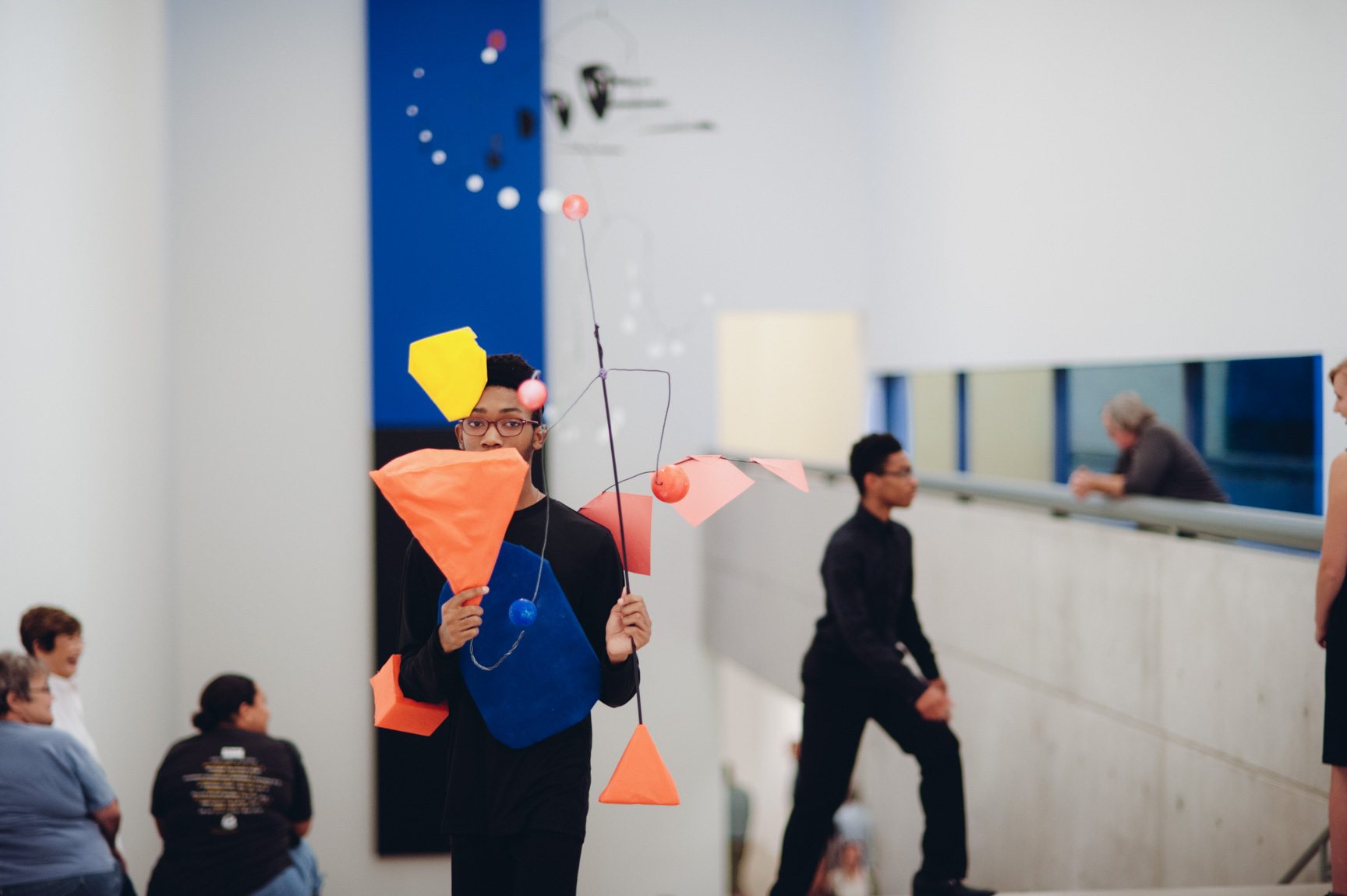 A student performs for an audience in the Main Gallery holding mobile inspired by Calder's work.