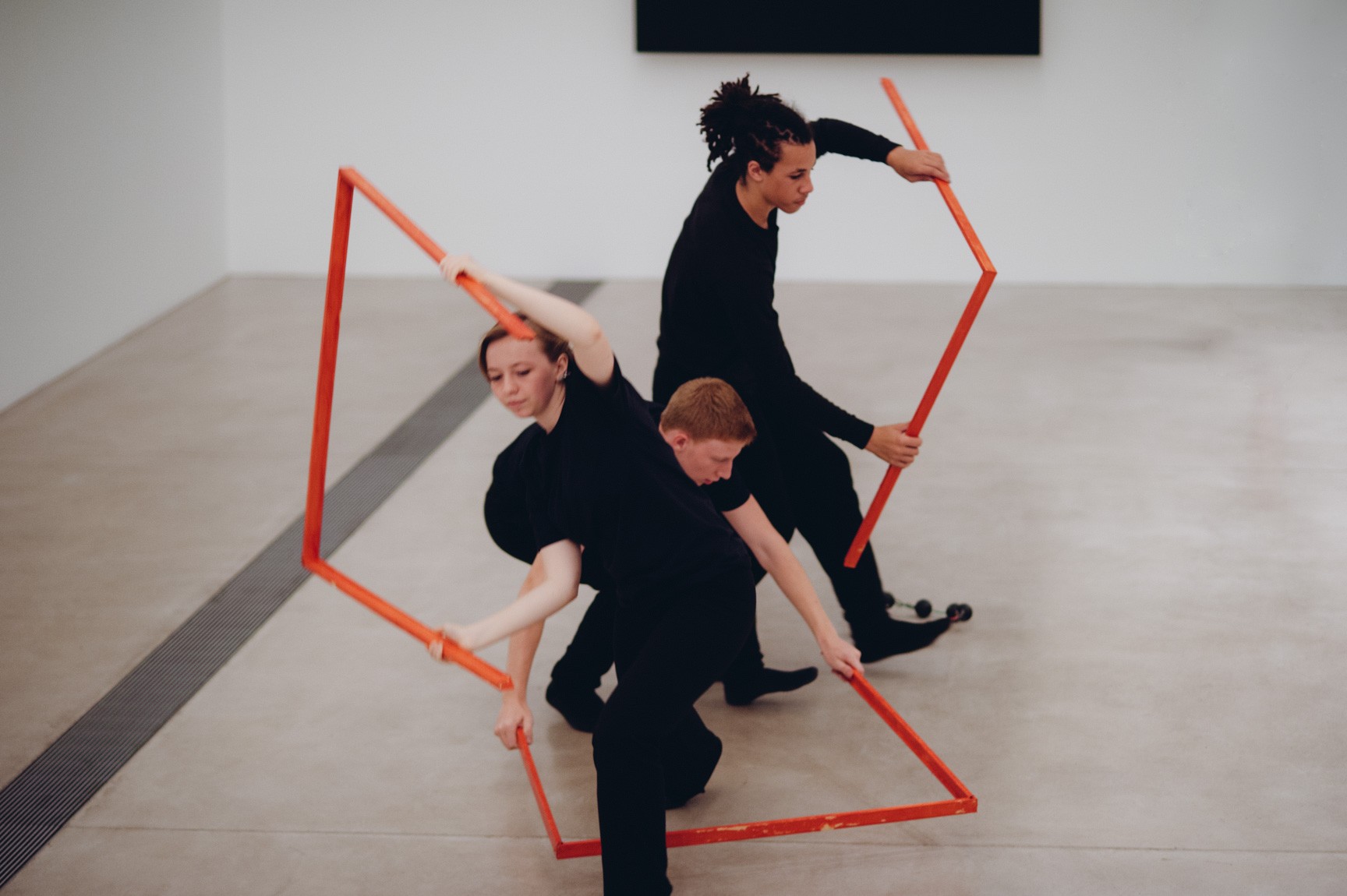 Three students perform in front of Kelly's "Blue Black," interweaving each other in red geometric shapes.