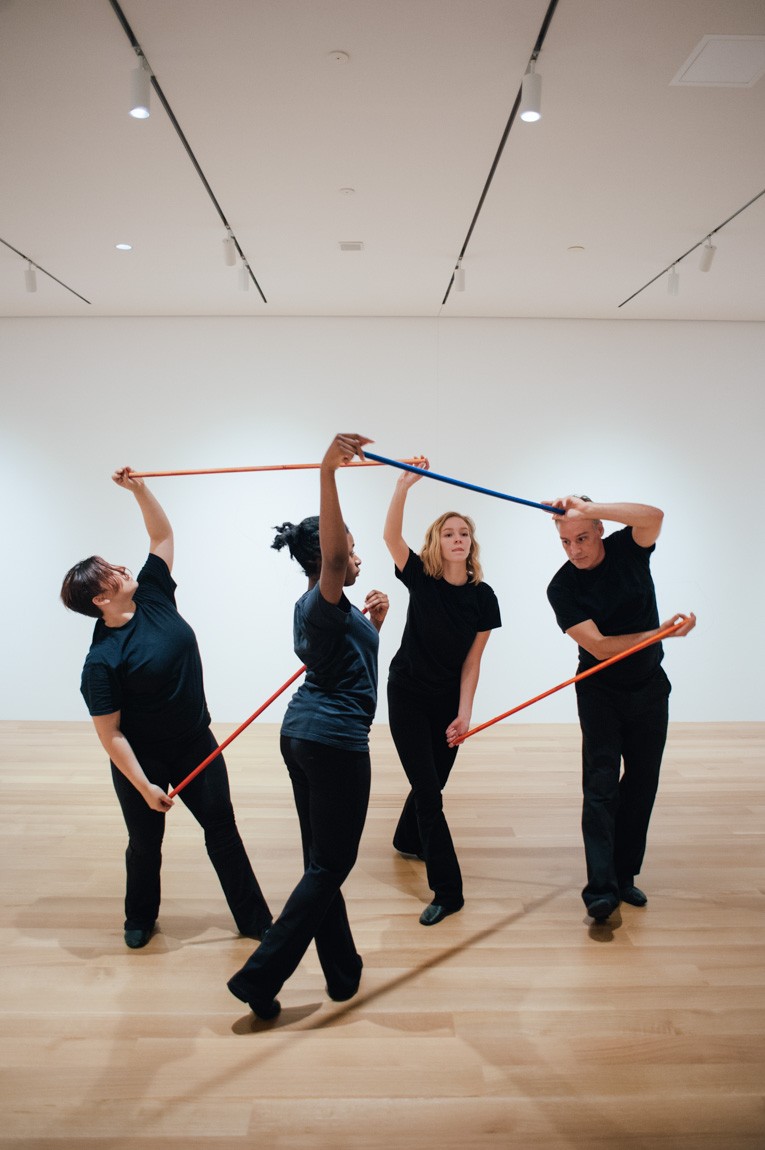 Four students perform the Lower-East Gallery holding colored sticks.