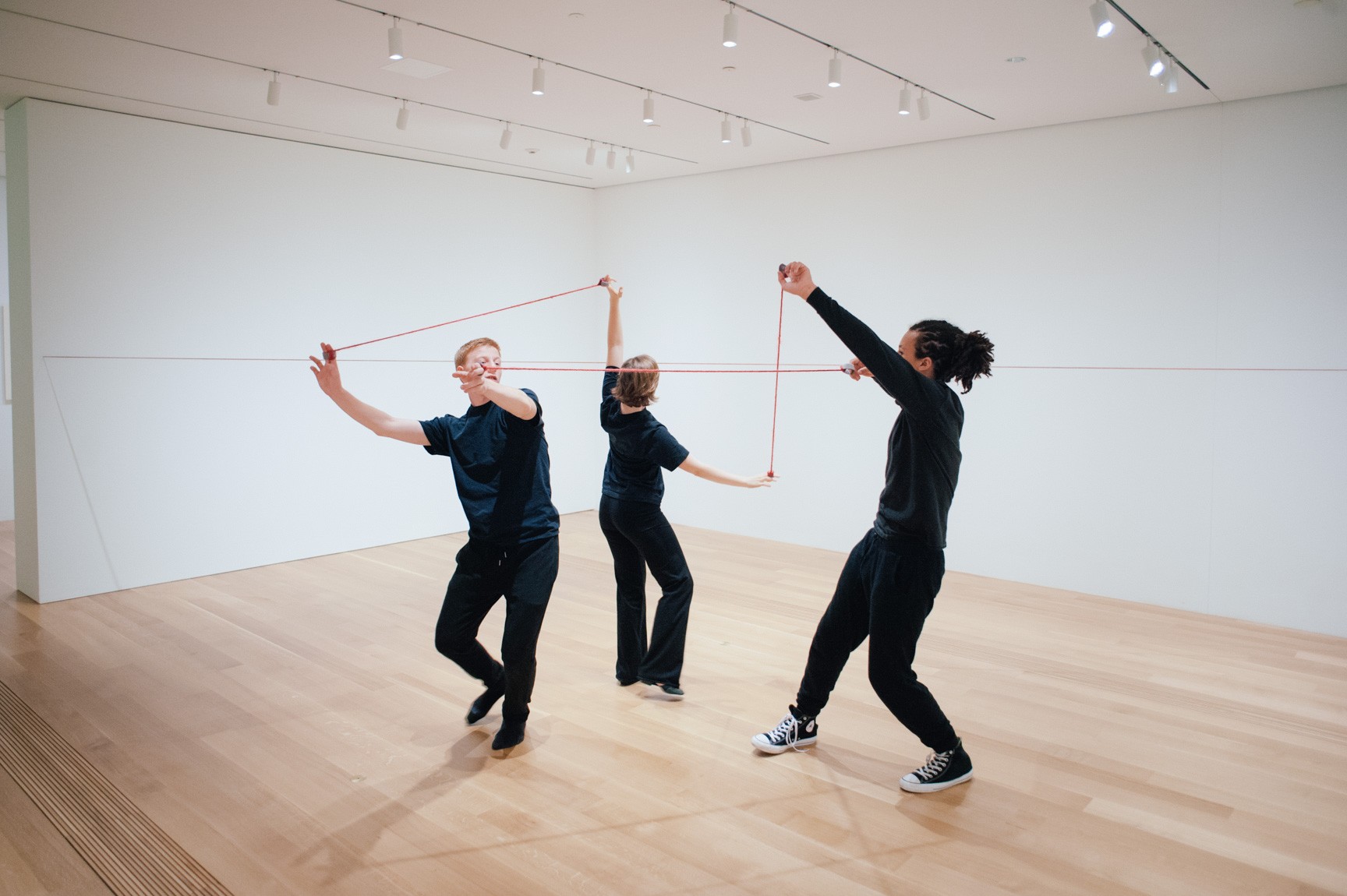 Three students perform the Lower-East Gallery with red ropes tied to their fingers.