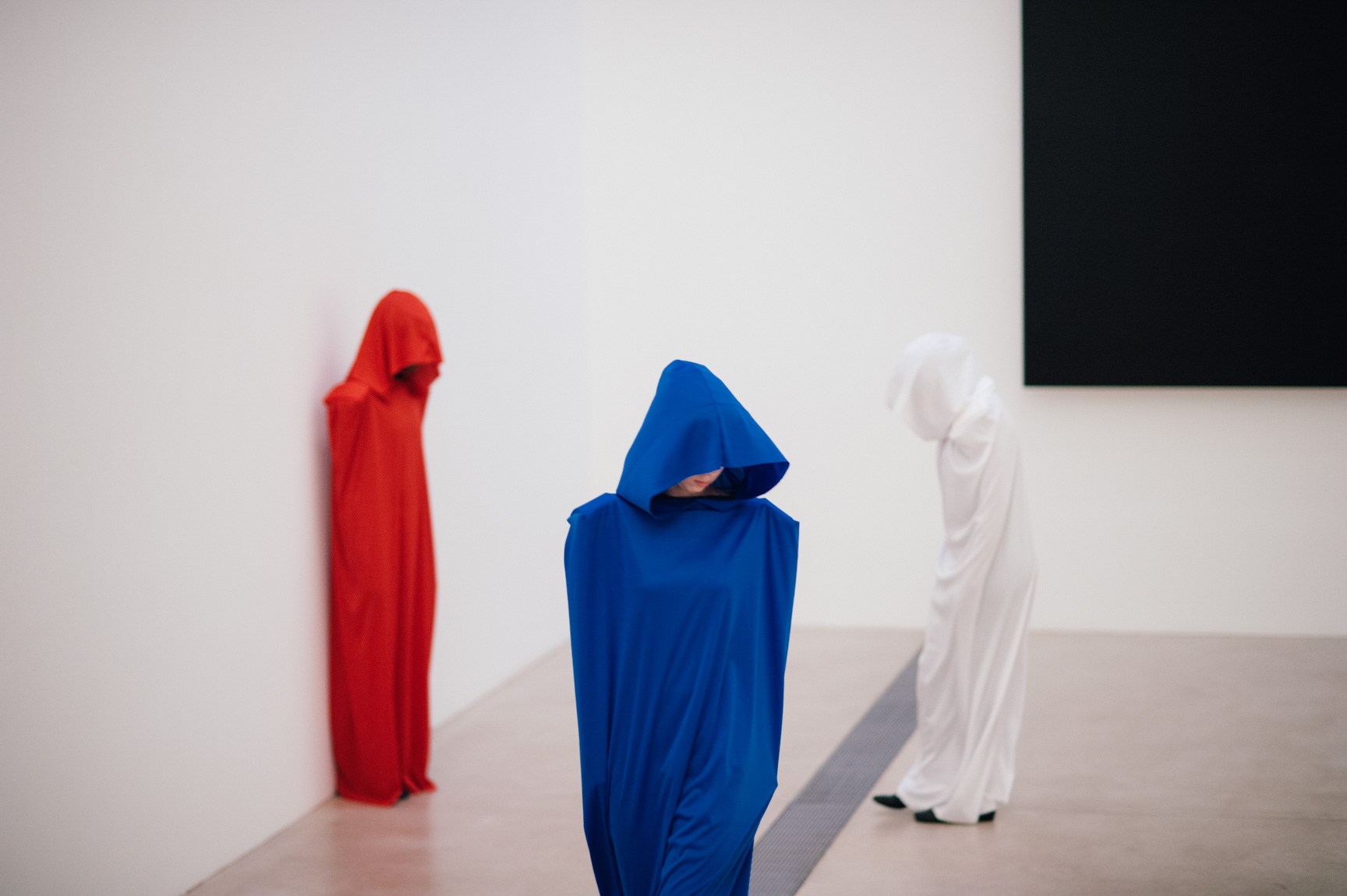 Three students perform wearing white, red, and blue hooded robes in front of Ellsworth Kelly's "Blue Black."