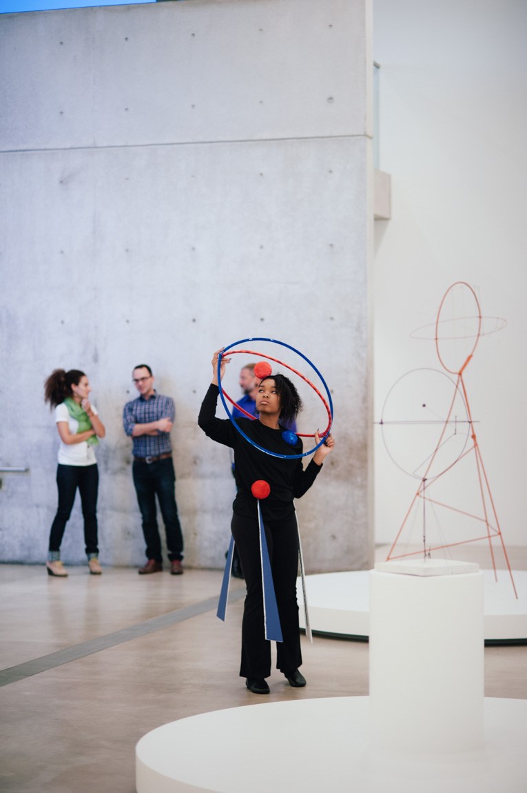 A student performs for an audience in the Main Gallery holding a sculpture inspired by Calder's work.