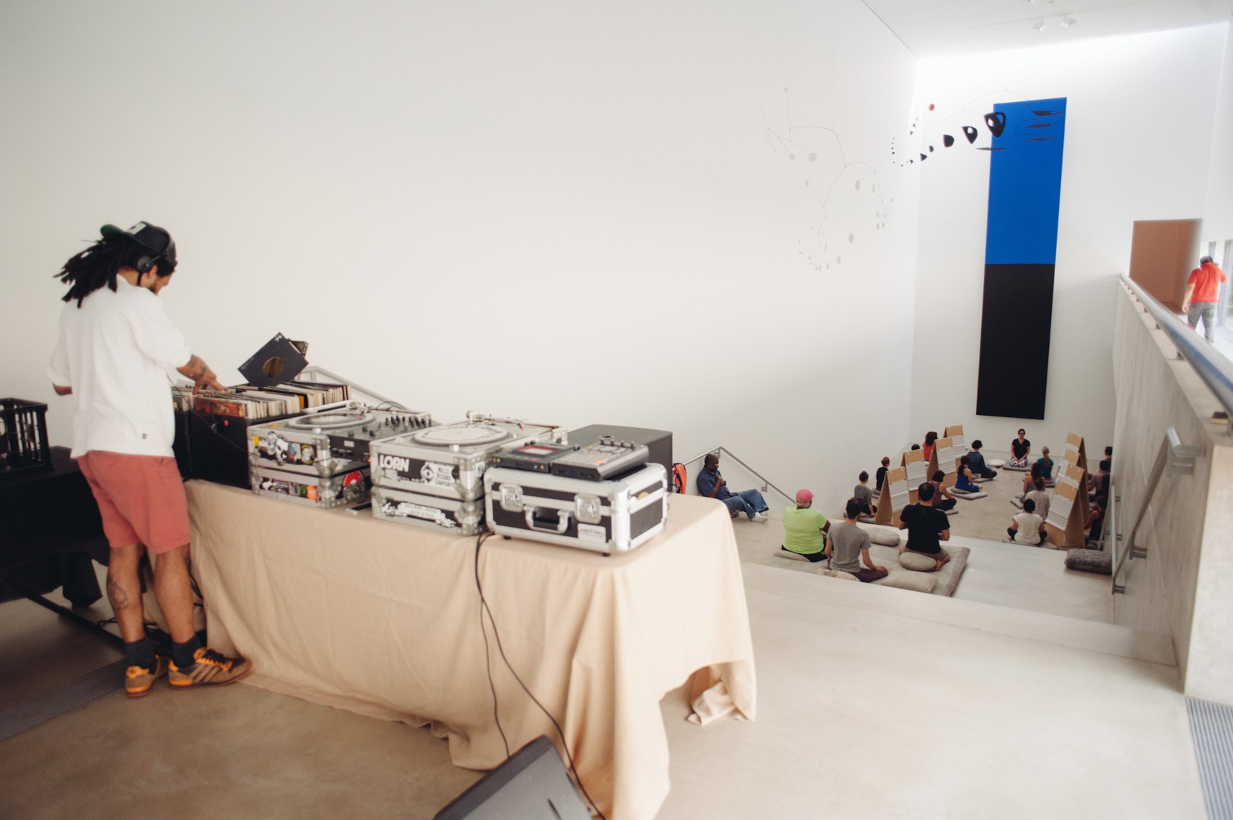 A view of Angela Malchionno leading participants in meditation in front of "Blue Black" by Ellsworth Kelly. A DJ sorts through records in the Main Gallery behind them.
