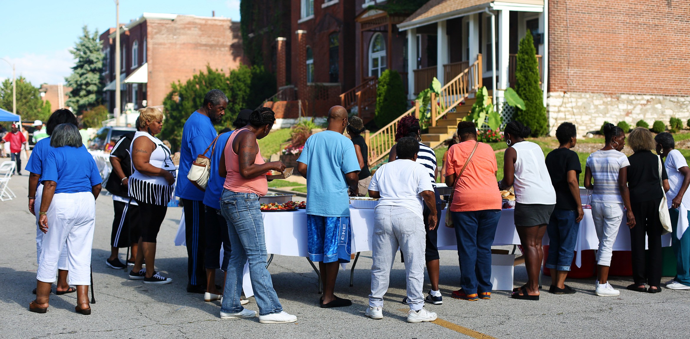A line of neighborhood members gathers around a lunch buffet.