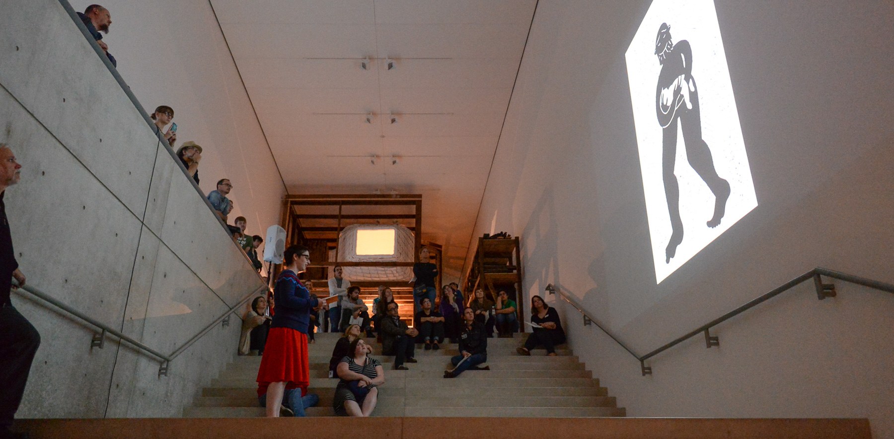 Marnie Galloway reads on the Main Staircase from her zine "Burrow" facing one of her illustrations projected on the wall.