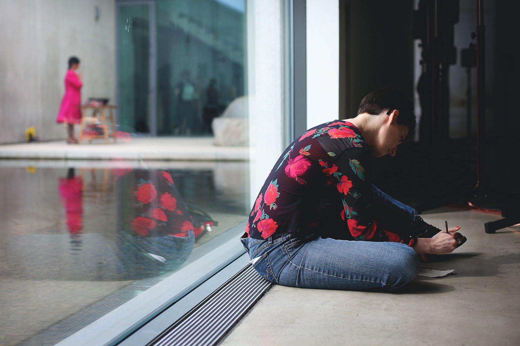 A visitor sits on the floor against a Main Gallery window adjoined with the Water Court, writing on a piece of paper.