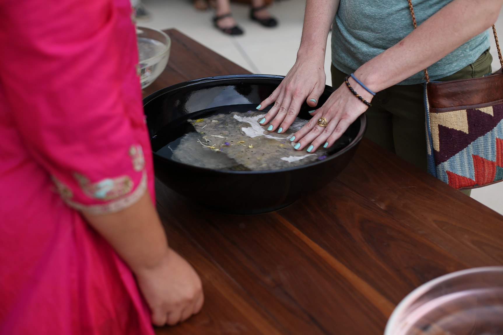 Closeup of a visitor's hands pressing handmade paper into a bowl of water, across from Bhanu Kapil.