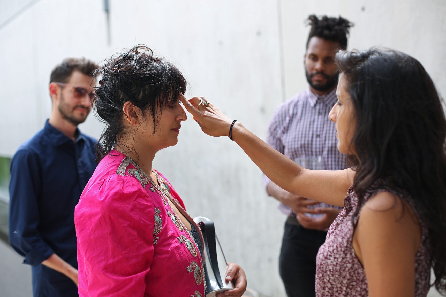 A collaborator performs a blessing and marks Bhanu Kapil's forehead in the Water Court as others observe.