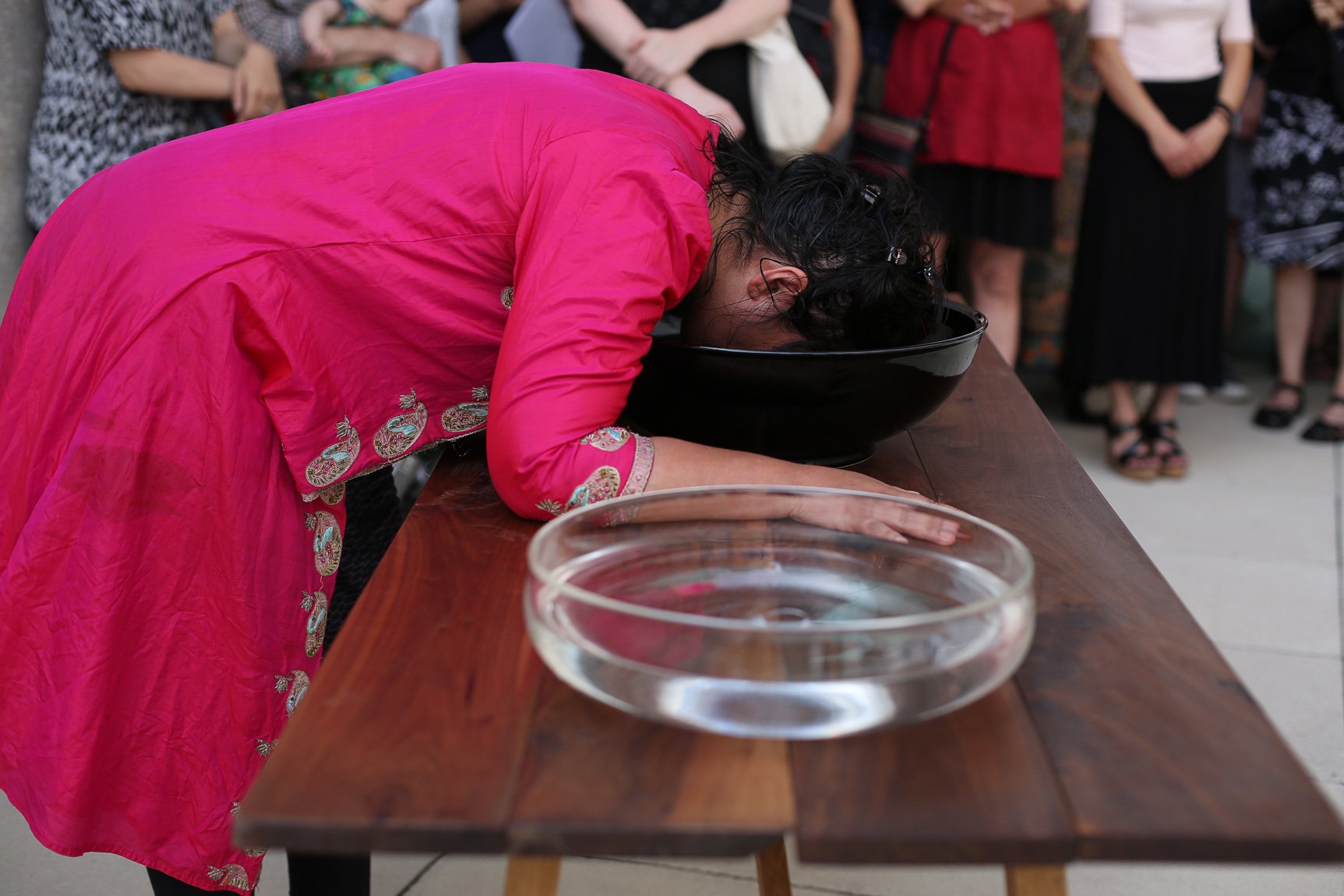 Bhanu Kapil brings her face down to dip into a bowl of water for an audience.