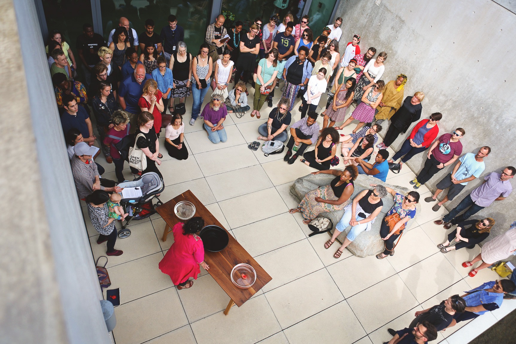 An aerial view of Bhanu Kapil performing a ritual in the Water Court for a large crowd.