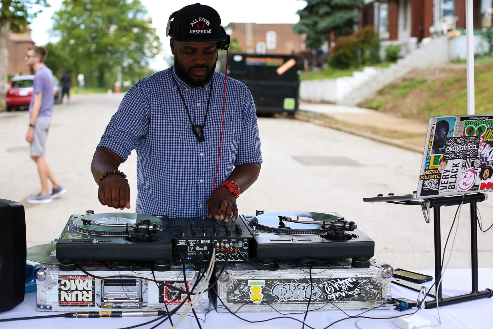 A DJ mixes behind turntables and a laptop for a neighborhood black party.