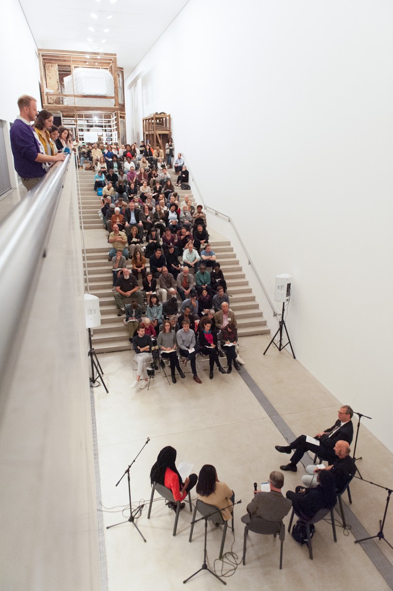 A large audience is seated on the Main Staircase, attending a panel discussion titled "Deconstructing and Reconstrucing St. Louis."