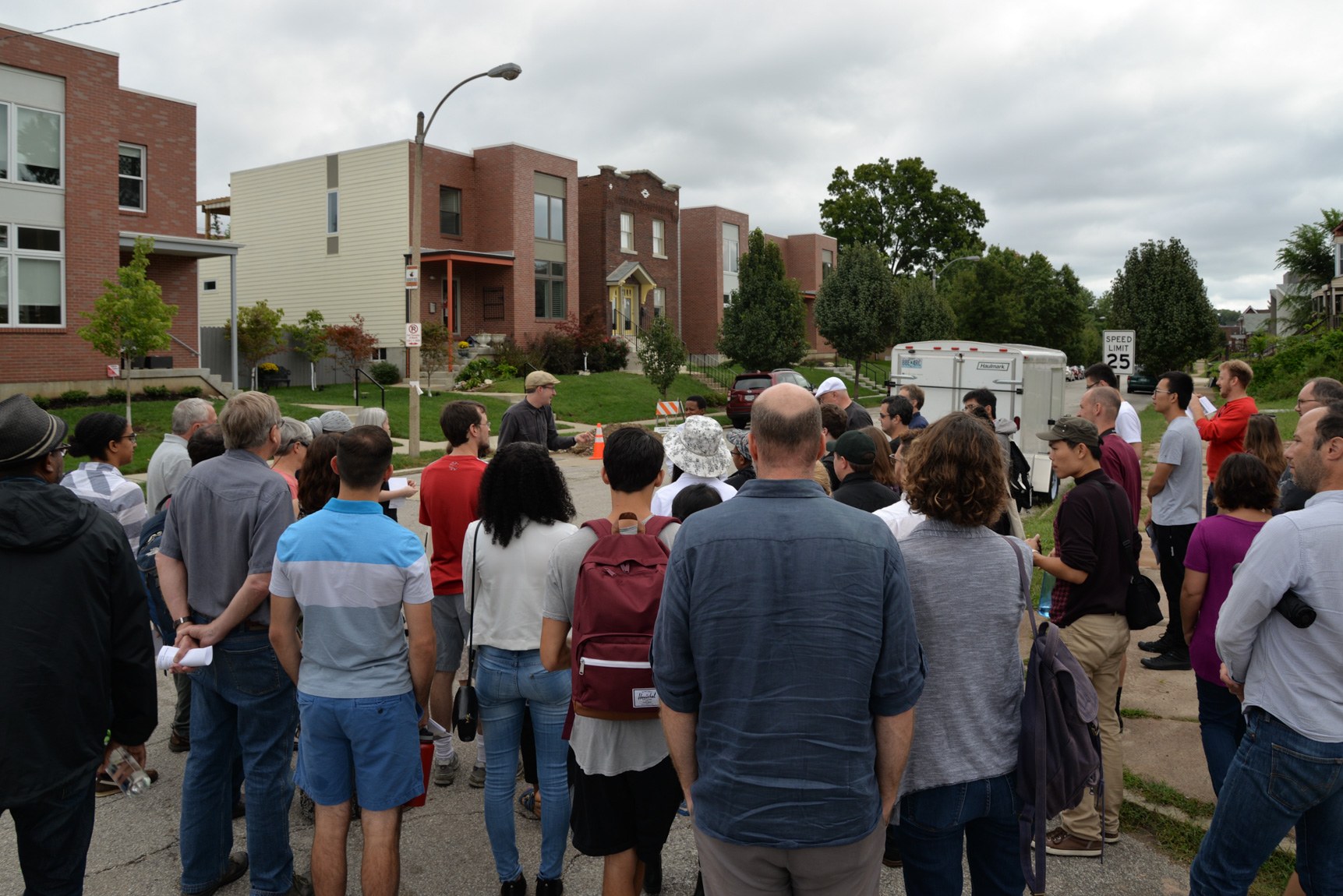 A large group gathers in a residential intersection listen to the tour leader.