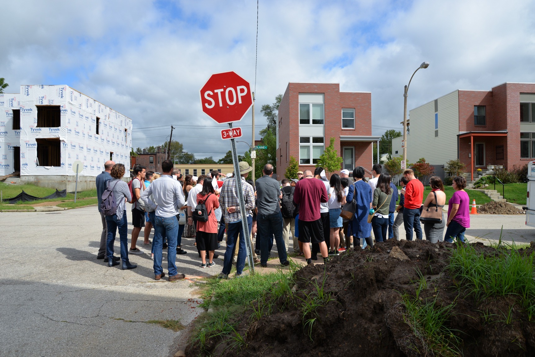 A large group gathers at in a residential neighborhood under construction by an intersection.