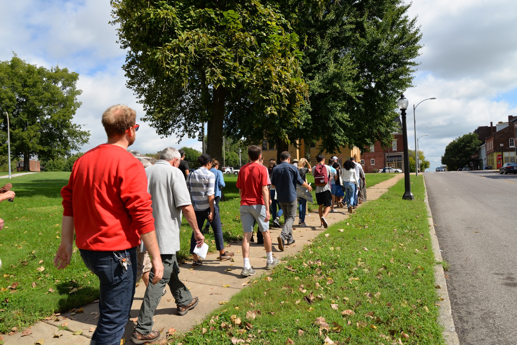 A line of field trip participants walks down a residential sidewalk on a sunny day.