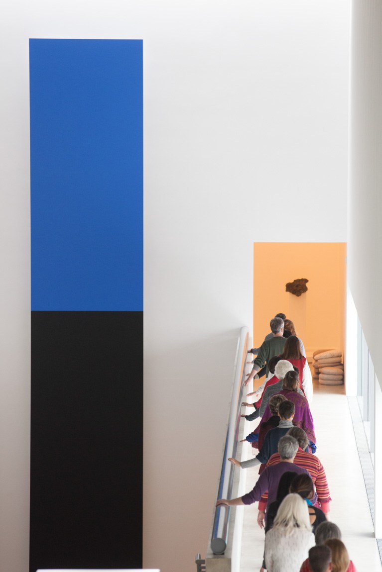 Workshop participants stand in a line to the Cube Gallery, holding the railing with their left hand. Ellworth Kelly's "Blue Black" hangs beside them.