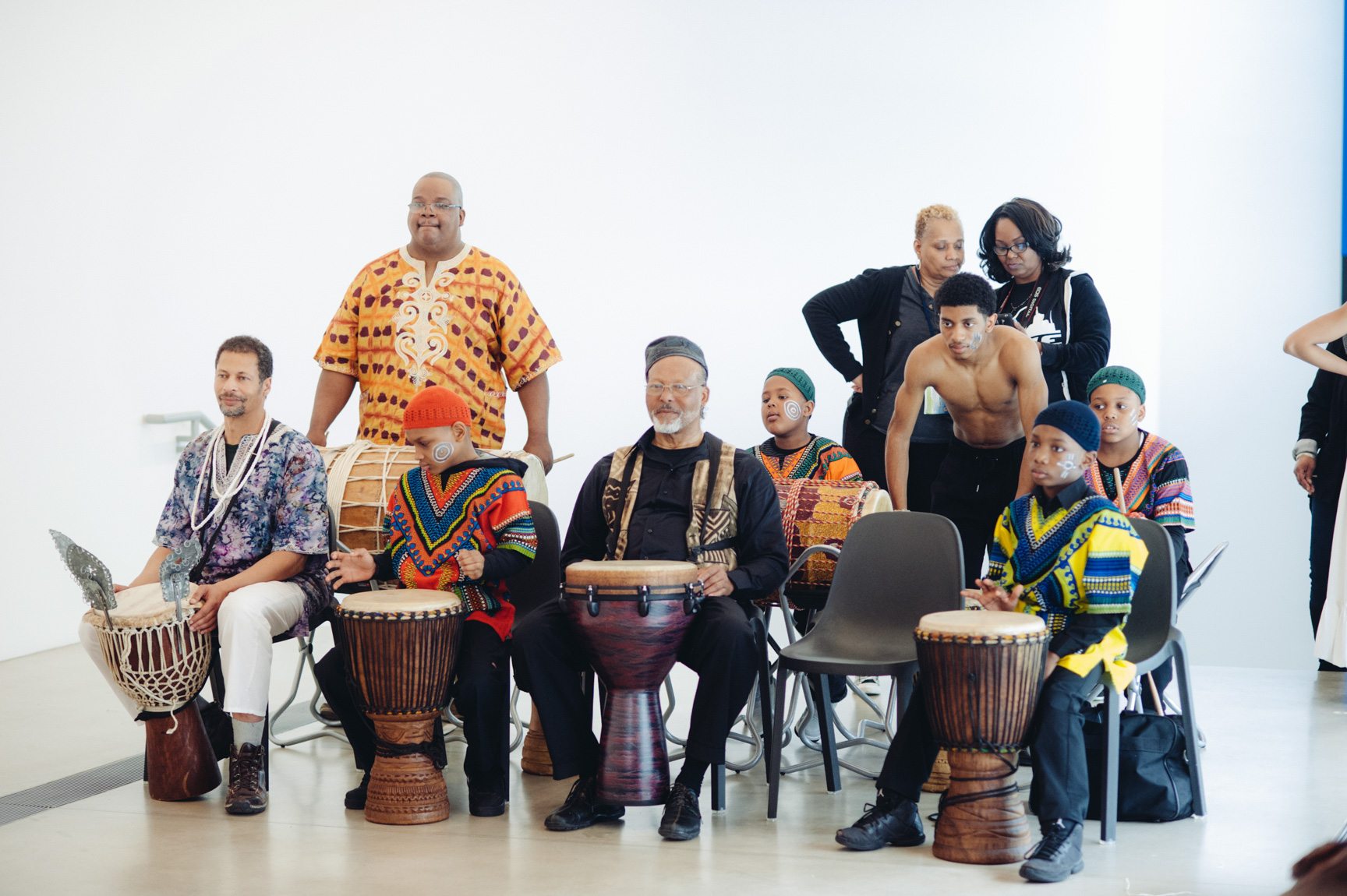 A group of djembe players sit behind their drums in the Main Gallery.