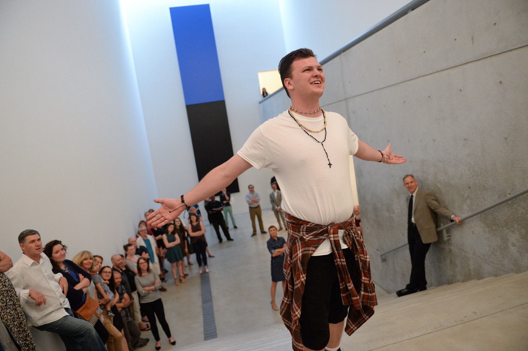 An actor performs with their arms outstretched in front of an audience lining the Main Staircase.