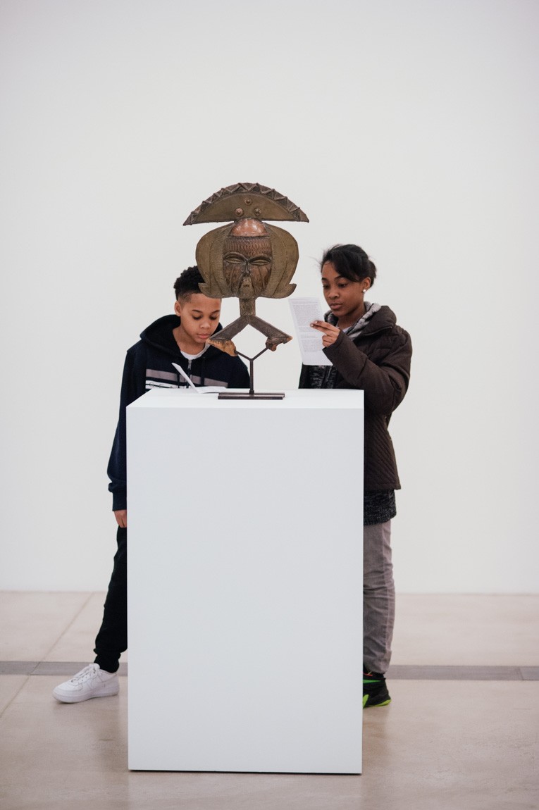 Two young visitors view an African sculpture.