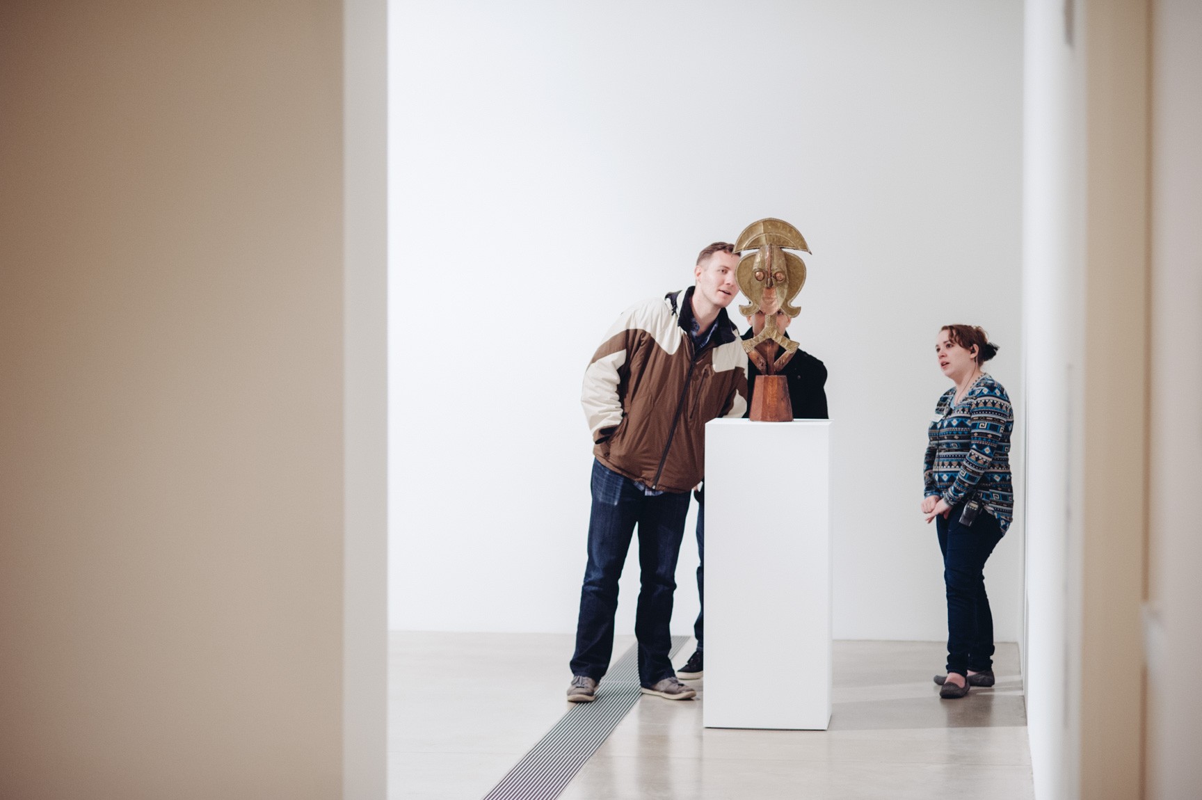 Two visitors admire an African sculpture as a gallery attendant watches over them.