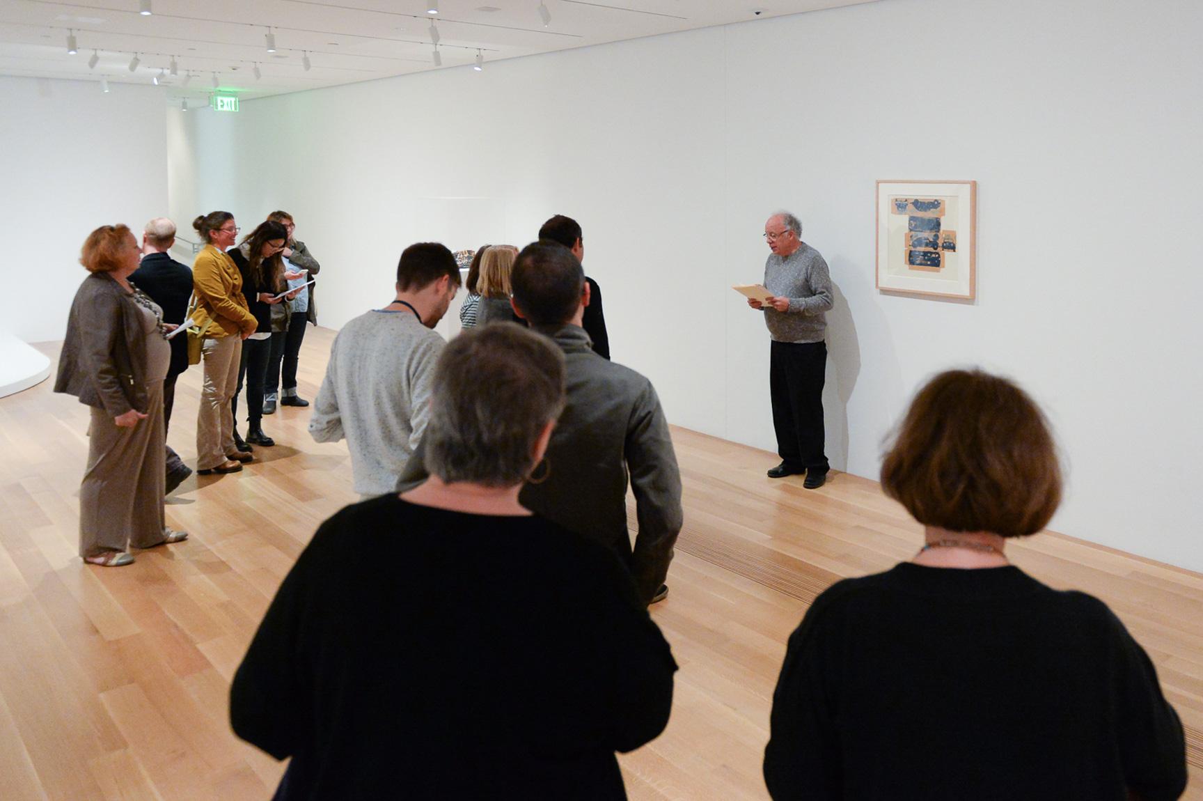 Buzz Spector gives a lecture in a lower-level gallery to an audience in front of Claes Oldenburg’s drawing, "The Airflow - Top and Bottom, Front, Back and Sides, to be Folded into a Box (Study for Cover of Art News)."