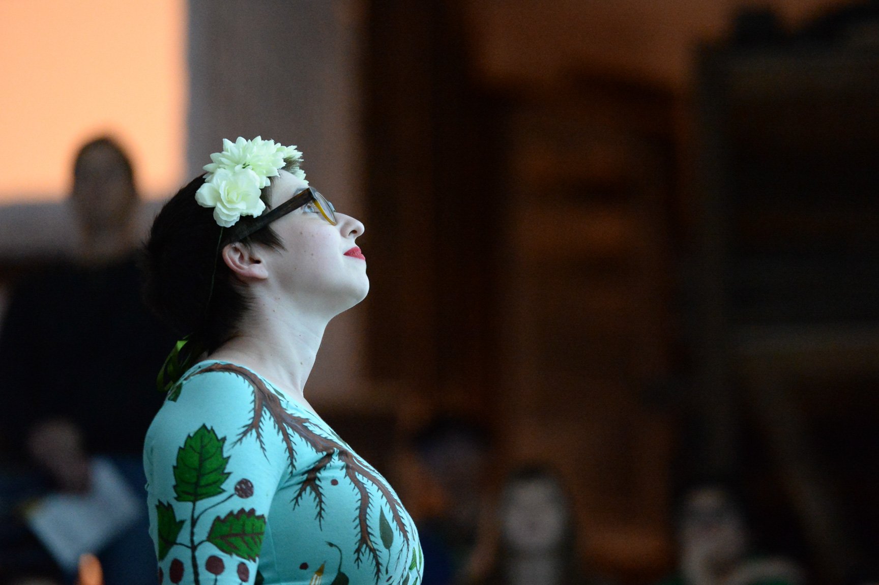 A presenter wearing a flower crown looks up at a bright image projected on the Main Staircase wall.