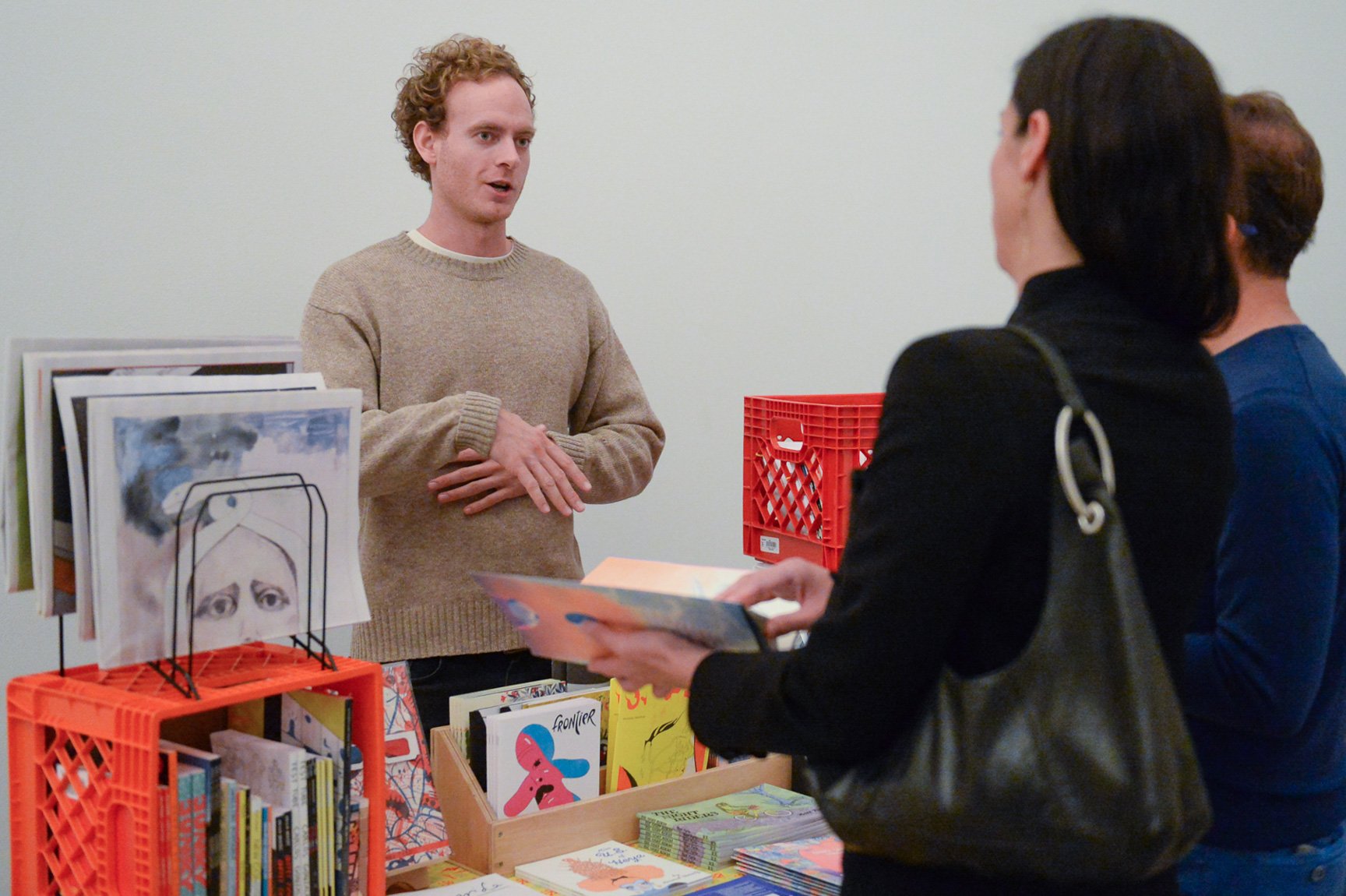 A vendor talks with visitors from behind their table filled with zines.