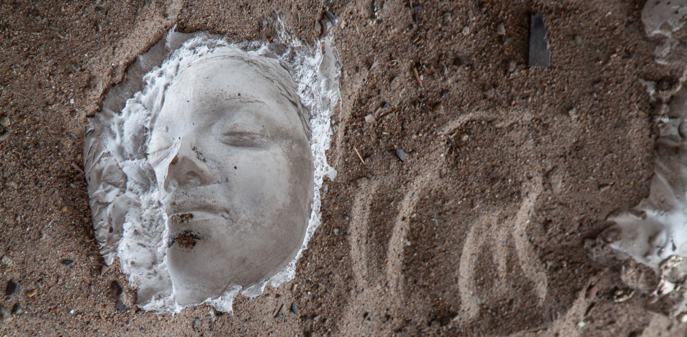 A closeup of a plaster sculpture of a face surrounded by dirt and sand.