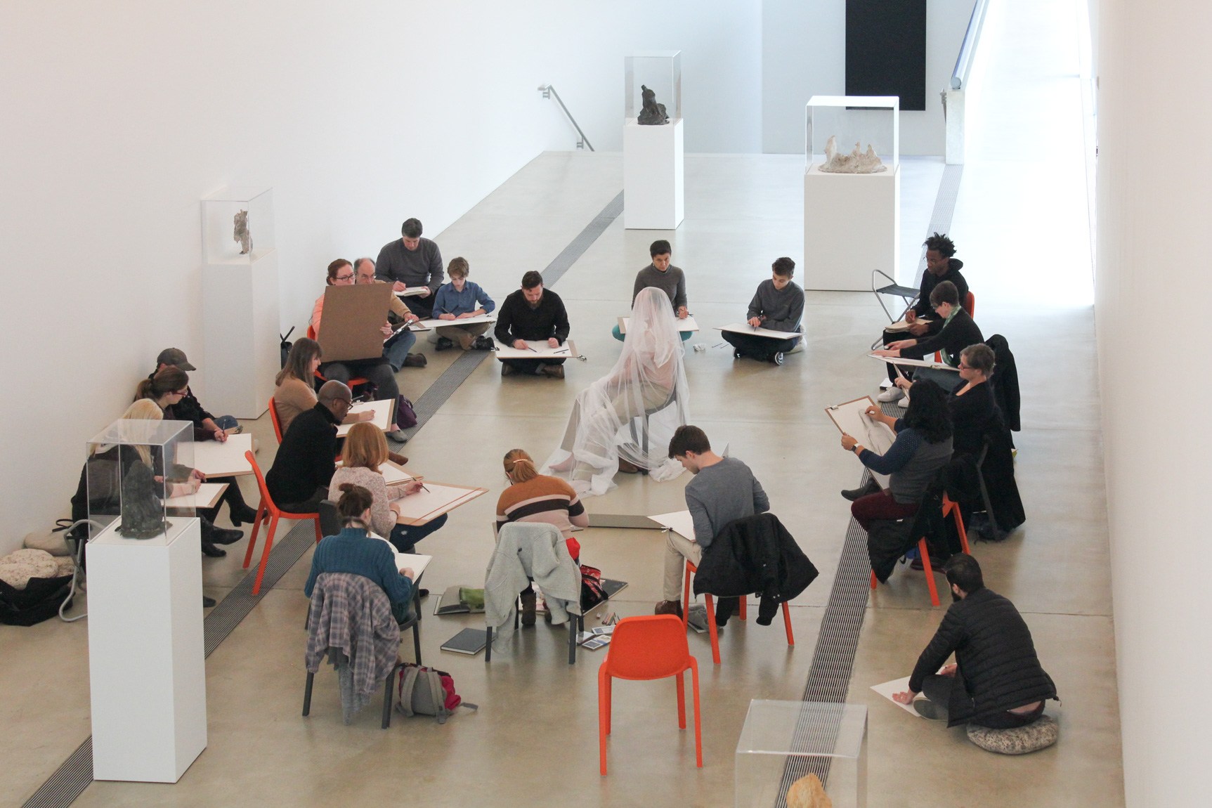A circle of artists sketch a seated model, covered in shear fabric in the Main Gallery.