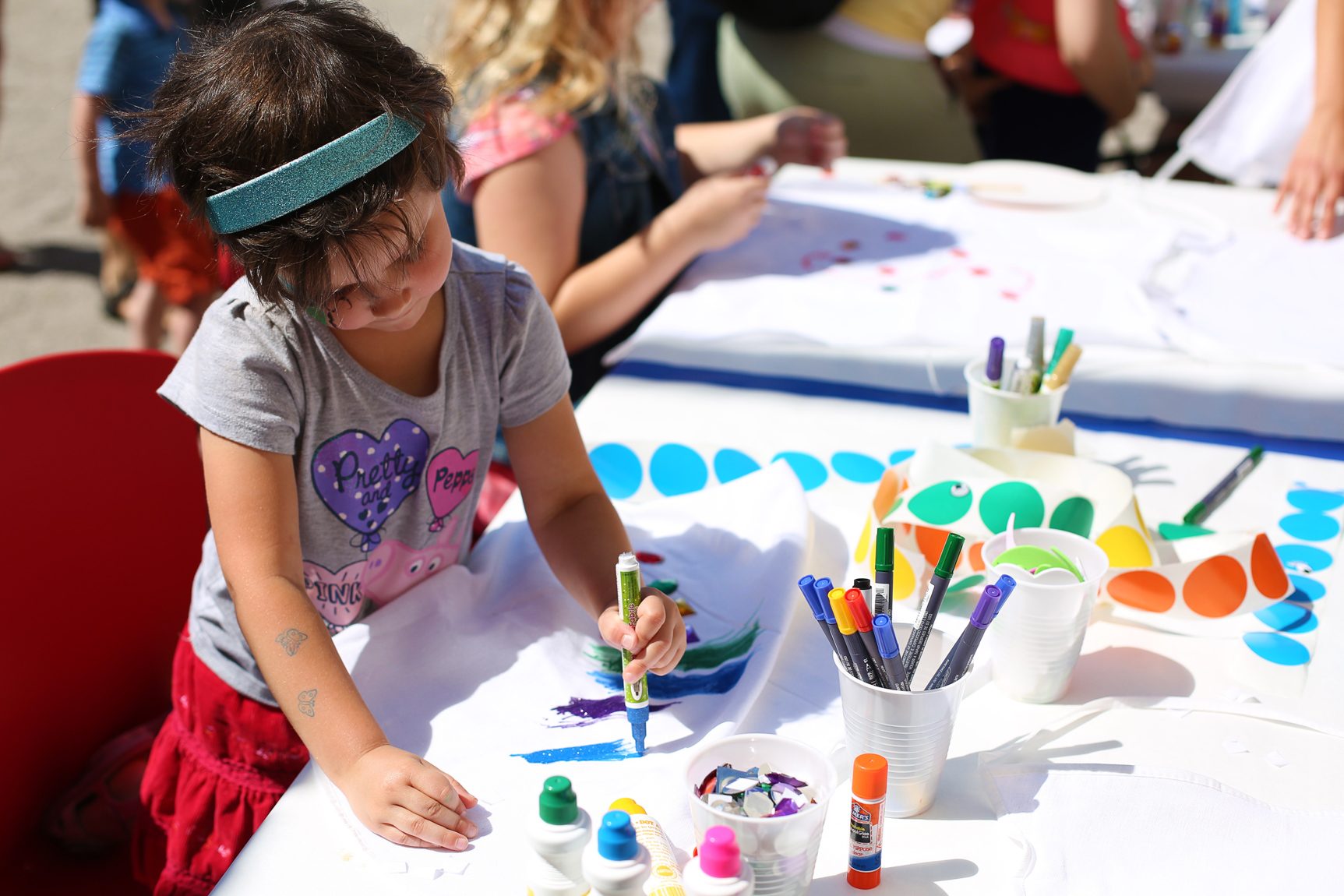 A child draws outside in the sun at a coloring station.