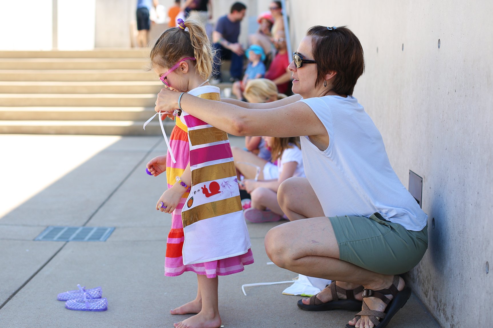 A parent ties a handmade cape around their child in the Courtyard.