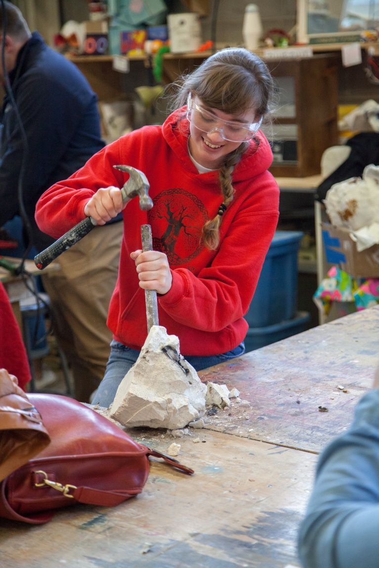 Webster student chisels a piece of plaster, revealing their sculpture.