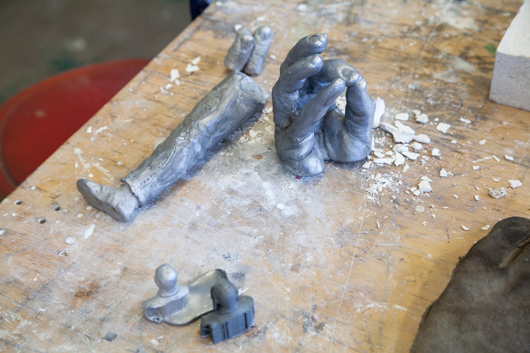 A worktable with metal sculptures of hands, a leg, and a small busts.