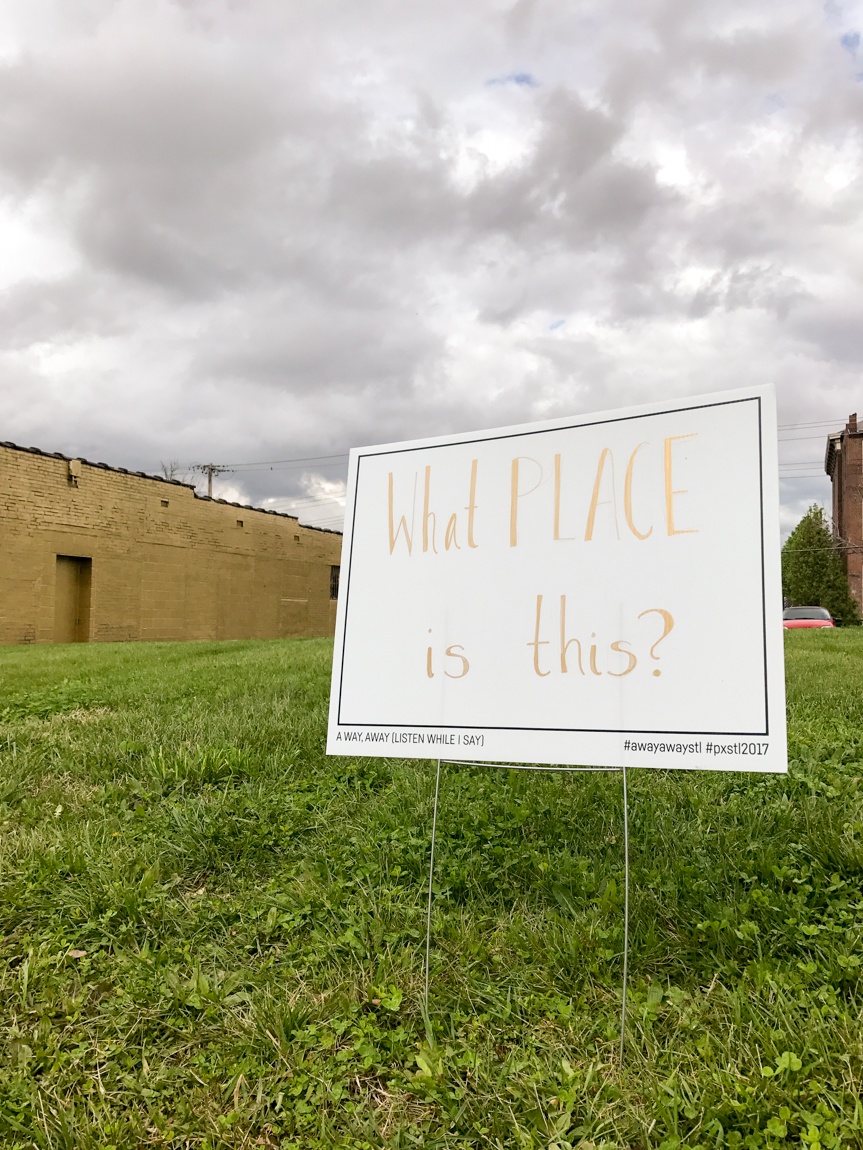 A white placard that reads "What PLACE is this?" sits in a lawn framed by a cloudy grey sky.