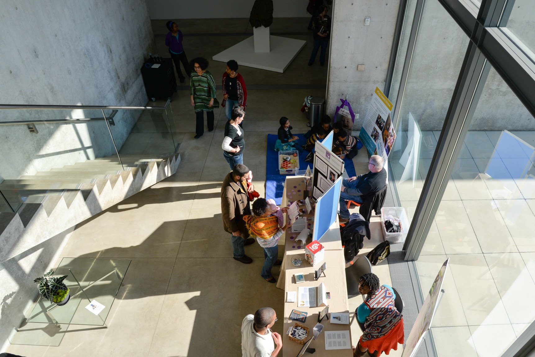 View from the Mezzanine of a group collected around a table with trifold boards in front of the Water Court windows.