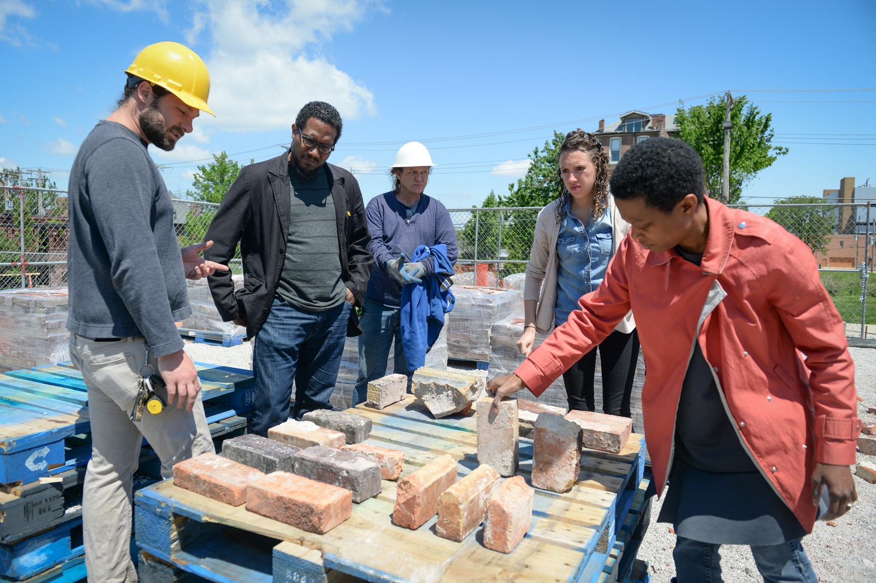 Amanda Williams, Andres L. Hernandez, and their team stand around a stack of pallets with a variety of bricks on it. Williams holds a brick upright on the pallet.
