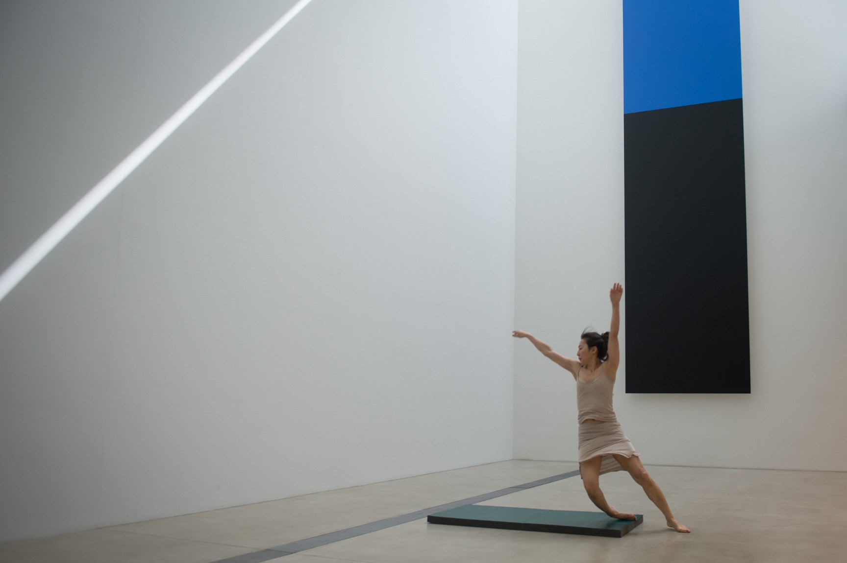 An AUNTS dancer wearing a flesh tone outfit performs in front of Ellsworth Kelly's "Blue Black" with a black crash mat.