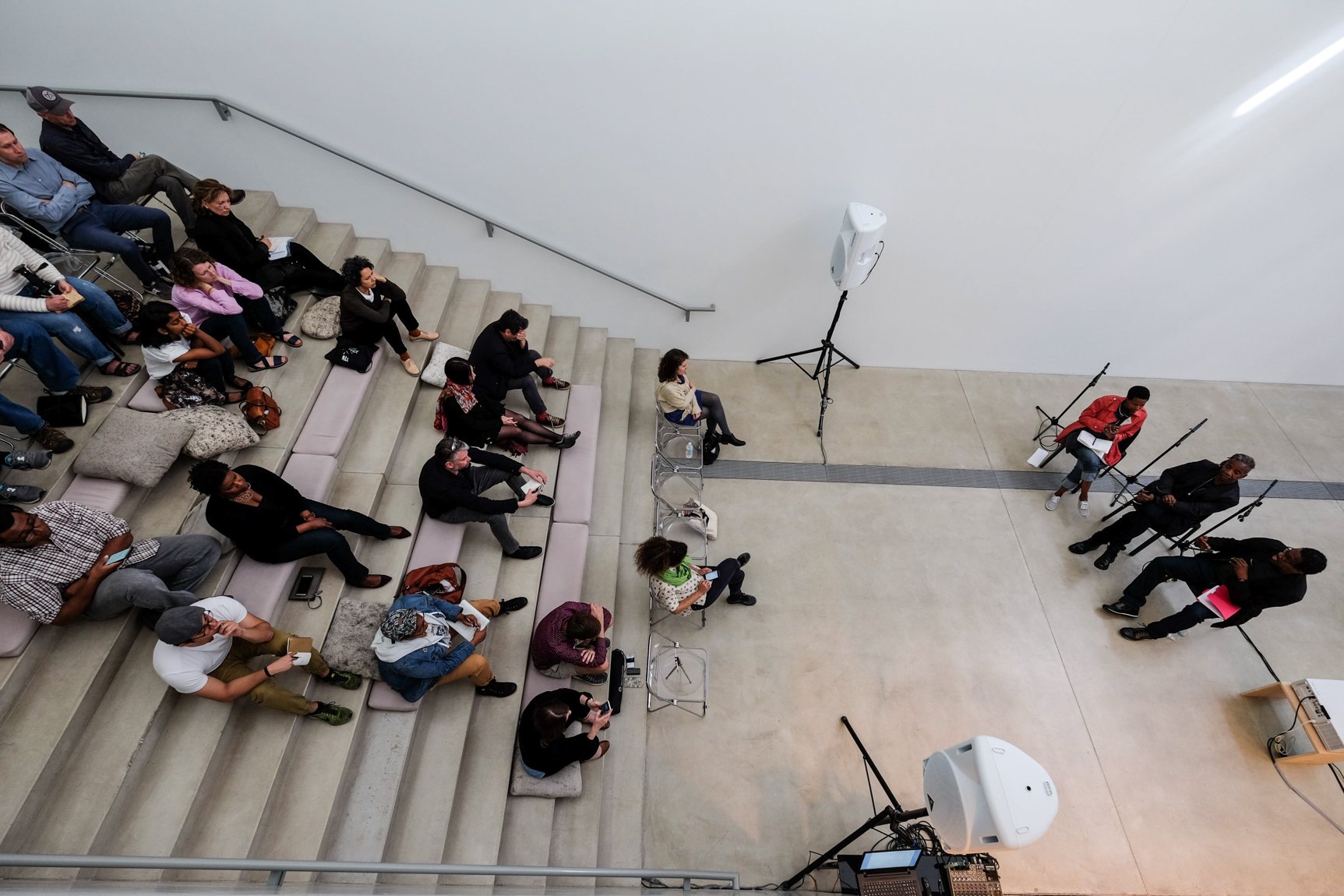 Aerial view of an audience seated on the Main Staircase and presenters talking from their chairs in the Lower-Main Gallery.