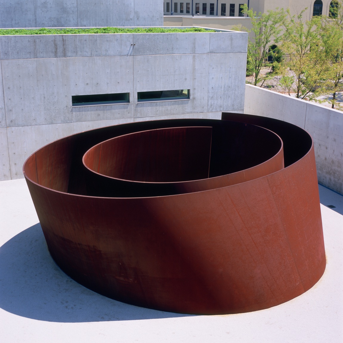 A sculpture by Richard Serra titled, Joe. An imposing spiral like a nautilus shell made of Cor-Ten steel is situated in a gravel courtyard next to the Pulitzer Arts Foundation building.