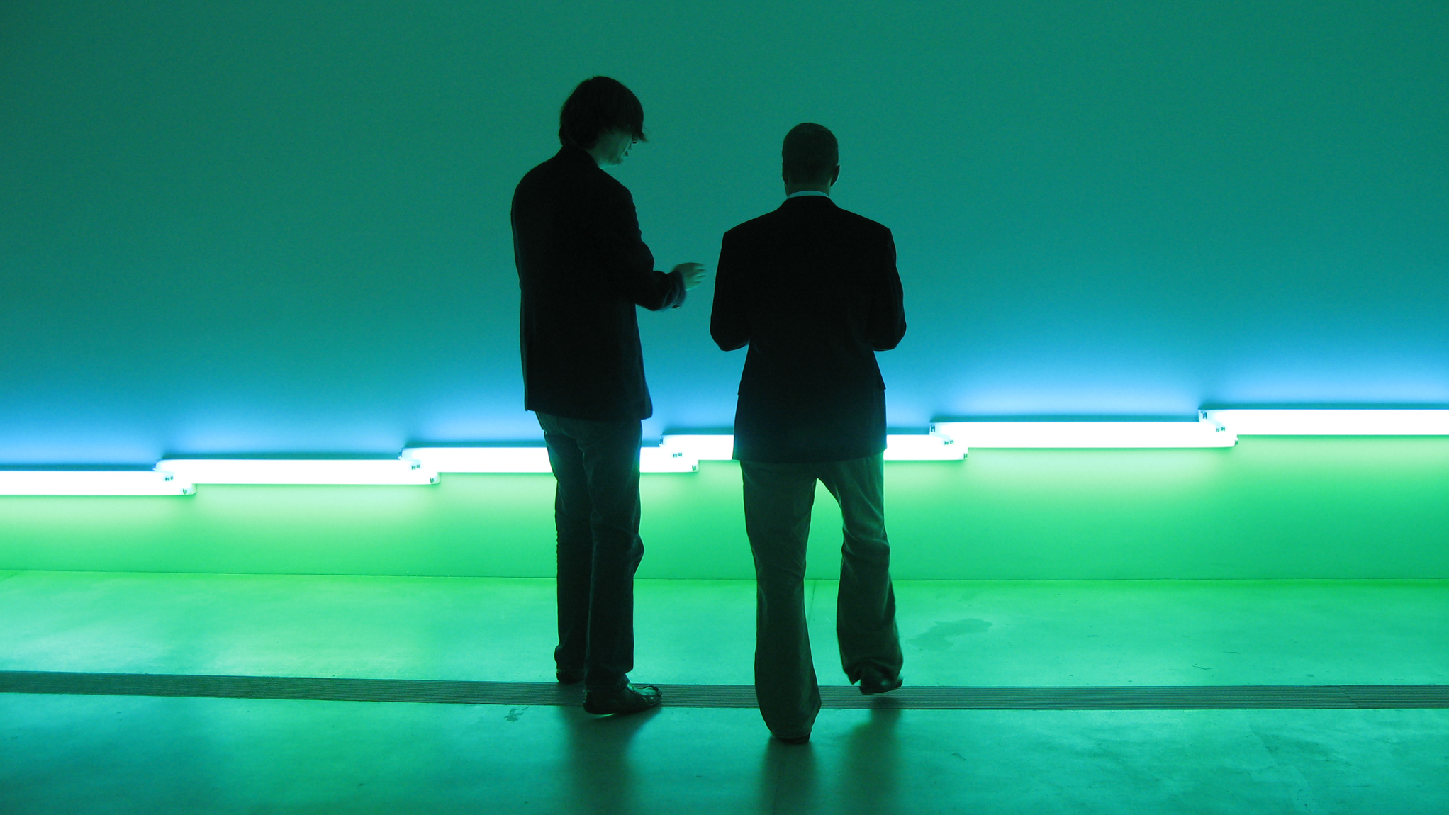 Steven Morse speaks to a professor about Flavin's glowing blue and green installation 