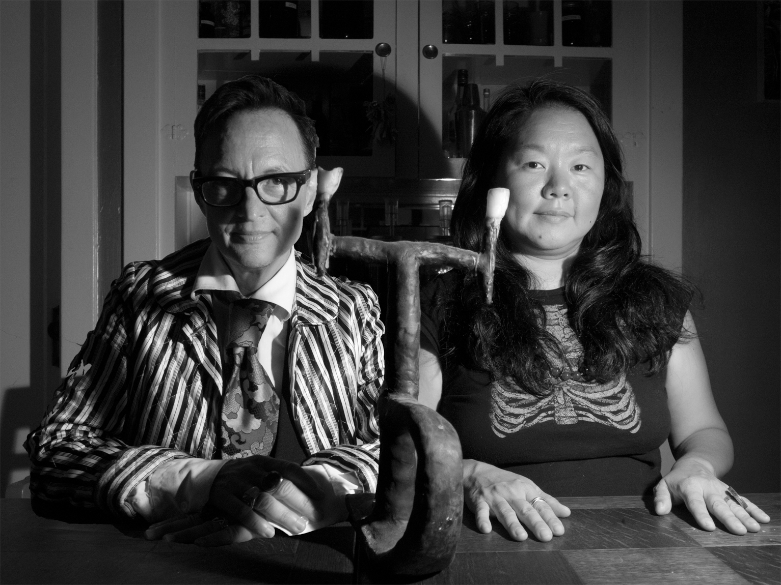 A black and white photograph of Asher Hartman and Haruko Tanaka seated at a table and looking into the camera.