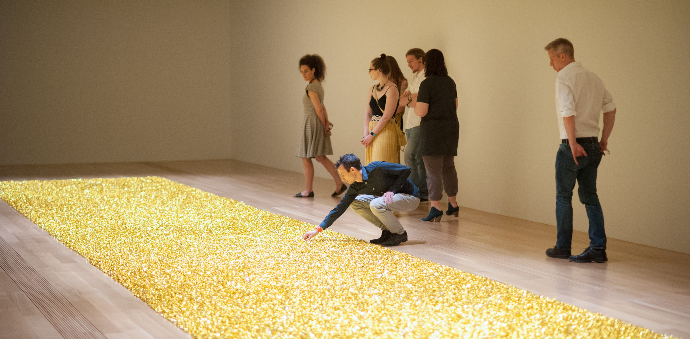 Visitors gather in the Lower East Gallery around a shimmering golden carpet of wrapped candies, an installation piece by Felix Gonzalez-Torres titled 