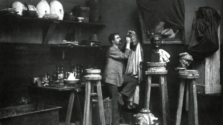 A black and white photograph of Medardo Rosso sculpting a bust in his studio.
